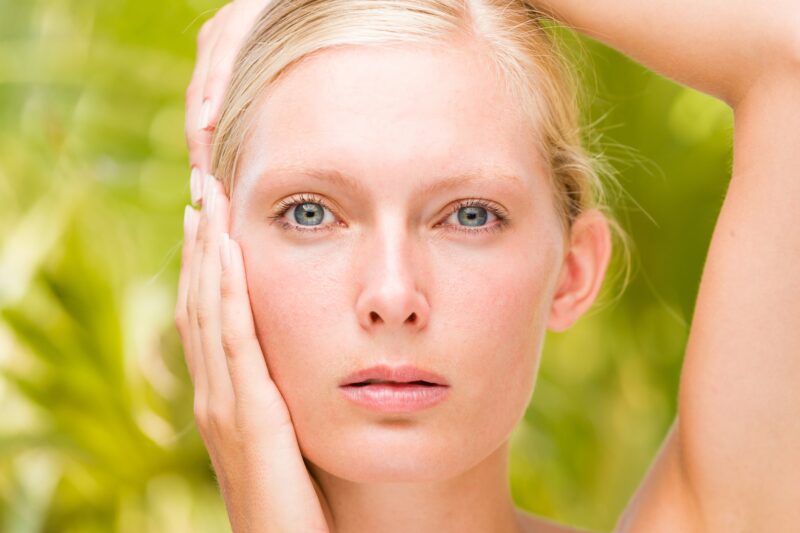 woman in nature touching her face to showcase environmental stressors to skin and skin care